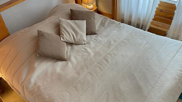 Un lit avec une couette beige et deux oreillers, une tête de lit en bois et une table de chevet avec une lampe.