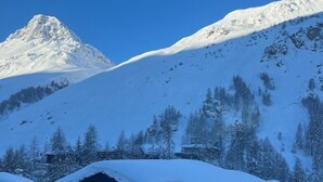 Una cabana de fusta amb un teulat cobert de neu, envoltada d'arbres plens de neu i una muntanya al fons.