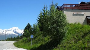 Une route avec un panneau de signalisation bleu, un bâtiment portant l’inscription « LES CASTORS », et des montagnes enneigées en arrière-plan.