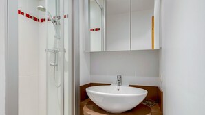 Une salle de bain moderne avec une douche à parois de verre, un lavabo blanc doté d’un plan de toilette marron et un miroir au-dessus du lavabo.