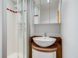 A modern bathroom with a glass shower enclosure, a white sink with a brown countertop, and a mirror above the sink.