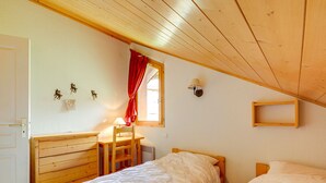 Une chambre à coucher avec une tête de lit en bois, un bureau avec une chaise, une fenêtre avec des rideaux rouges et une lampe fixée au mur.