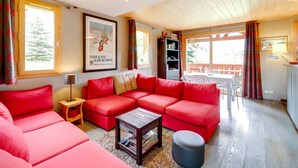 Un salon avec un canapé d’angle rouge, une petite table en bois et une bibliothèque.