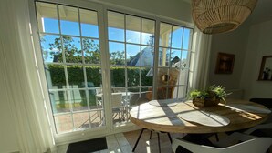 Een eetgedeelte met een ronde tafel, witte stoelen en een uitzicht door grote glazen deuren op een terras.