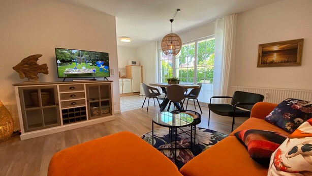 Een woonkamer met een televisie, bank, stoelen en een eethoek met een tafel en stoelen.