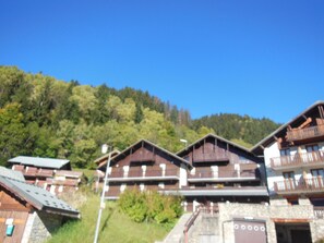 A row of wooden buildings with balconies, set against a backdrop of green hills. - Cozy studio in Champagny-en-Vanoise, for 4 people, south-facing balcony, pets allowed (Champagny-en-Vanoise)