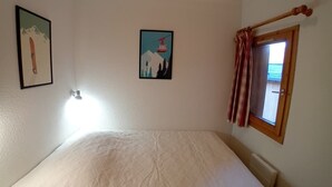 A room with a bed, a window with curtains, and two framed pictures on the wall.