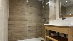 A modern bathroom with a wooden wall, a glass shower enclosure, and a white sink with a wooden vanity.