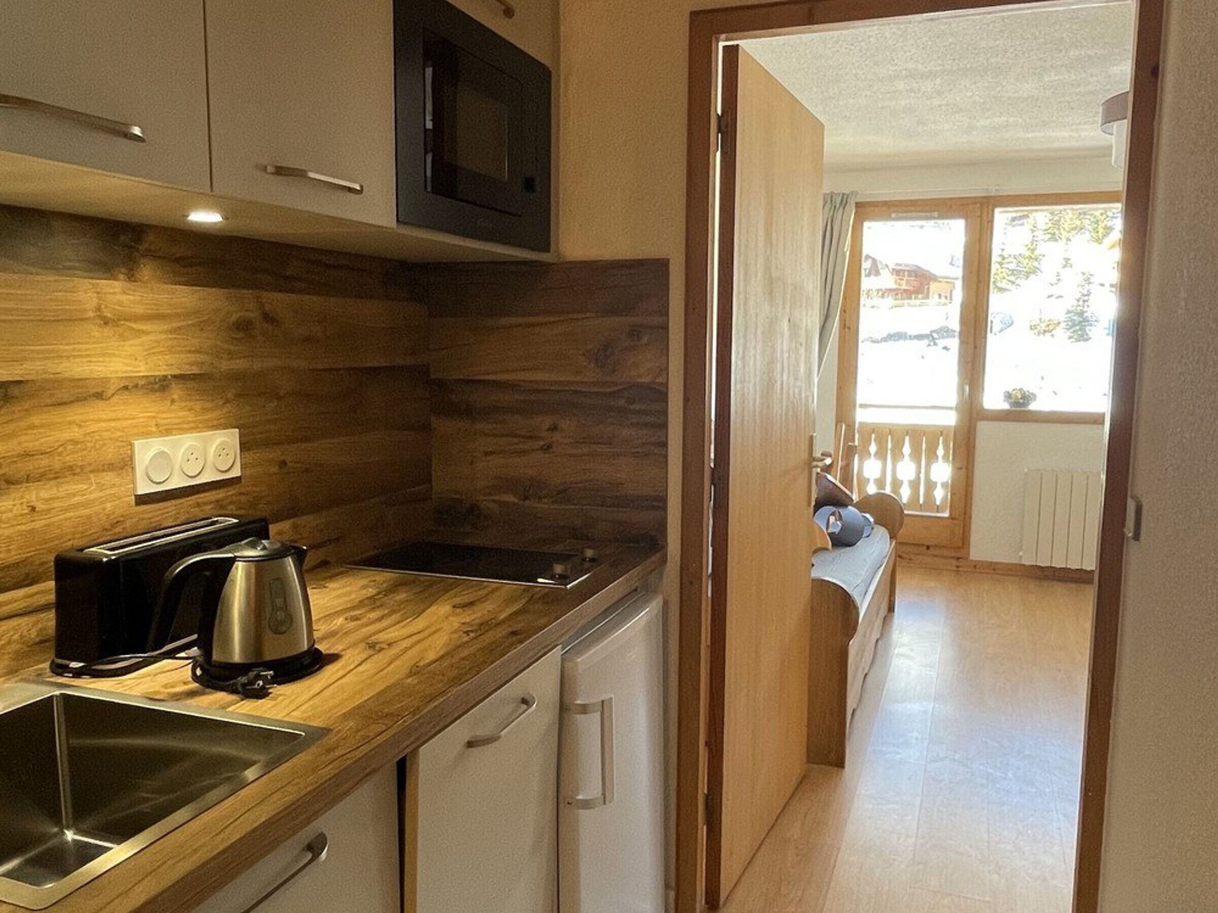 A compact kitchen with wooden cabinetry, a built-in microwave, a toaster, and a sink.