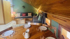 A cozy room with a wooden ceiling, a sofa with cushions, a dining table set with plates and glasses, and a lamp on a side table. - 3-room apartment for 6 in Méribel Altiport, near ski slopes (Méribel)