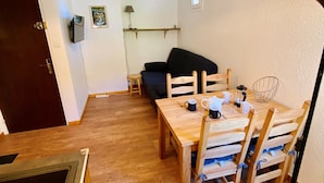 Un coin repas avec une table et des chaises en bois, un canapé noir et un petit tabouret.