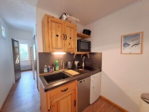Ett kompakt kök med träskåp, en mikrovågsugn, en diskho och en diskmaskin.