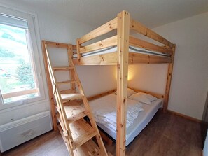 En våningssäng med en trästege, ett fönster med utsikt över träd och en vit dörr.