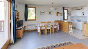 A cozy, well-lit room with a dining area, kitchen, and a TV. - Charming 4-room duplex, 8 people, west-facing terrace, near slopes (Peisey-Vallandry)