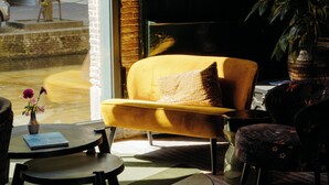 Una habitación con un ventanal grande, un sillón amarillo, una mesa redonda y una planta en maceta.
