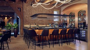Zona de bar con pared de ladrillo, vigas de madera en el techo y mostrador con taburetes.