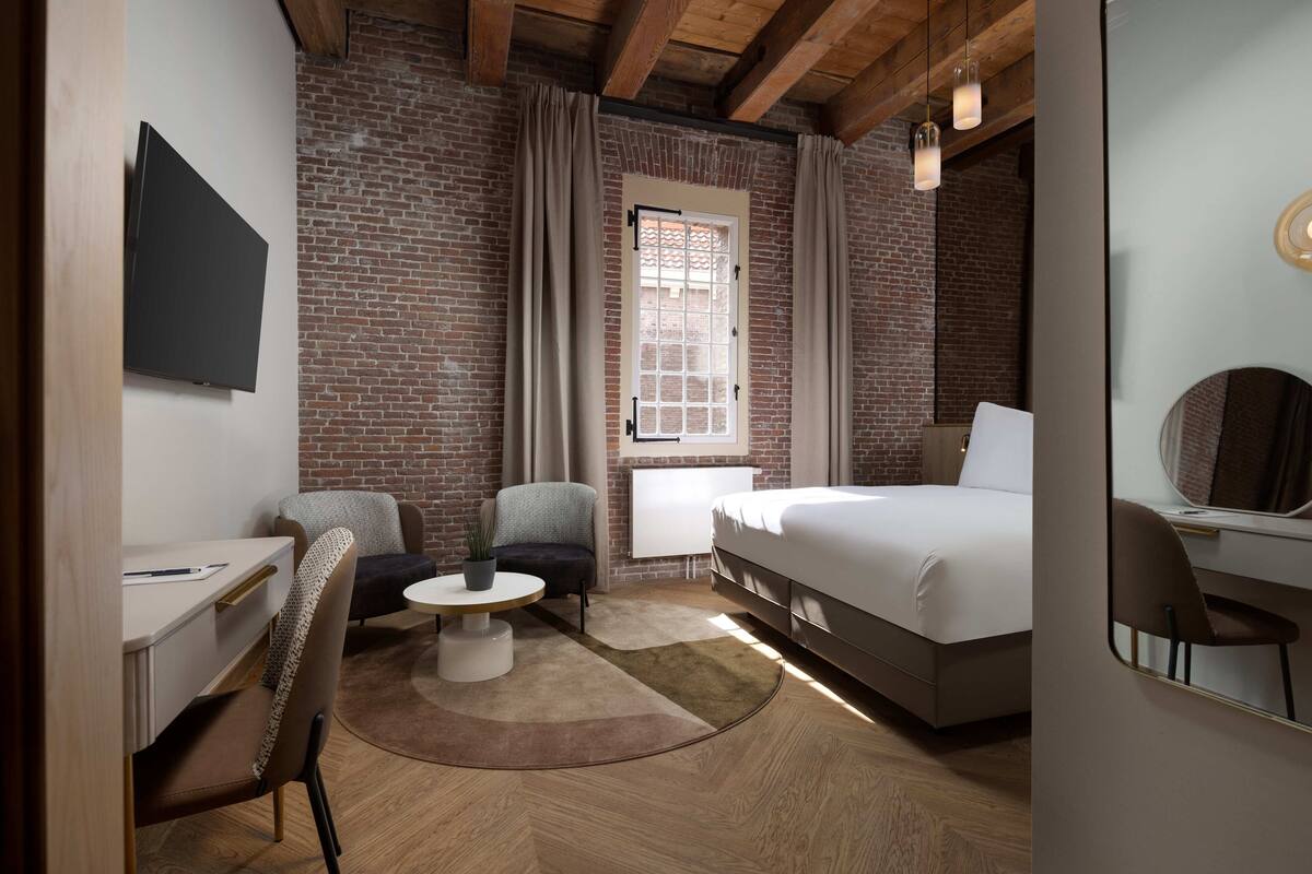 Una habitación de hotel moderna con pared de ladrillo, una cama, un escritorio y una silla.