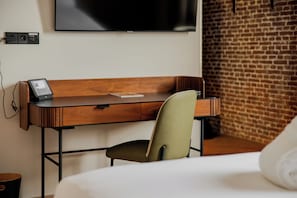 A hotel room with a wooden desk, a modern chair, a flat-screen TV mounted on the wall, and a brick wall. - Hotel Arsenaal Delft (Delft)
