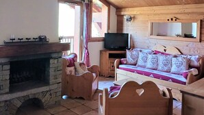 Una habitación acogedora con chimenea, muebles de madera, televisión y un sofá con cojines estampados.