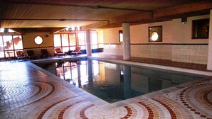 Una piscina interior con suelo de baldosas con círculos concéntricos, sillones de descanso y vistas al exterior.