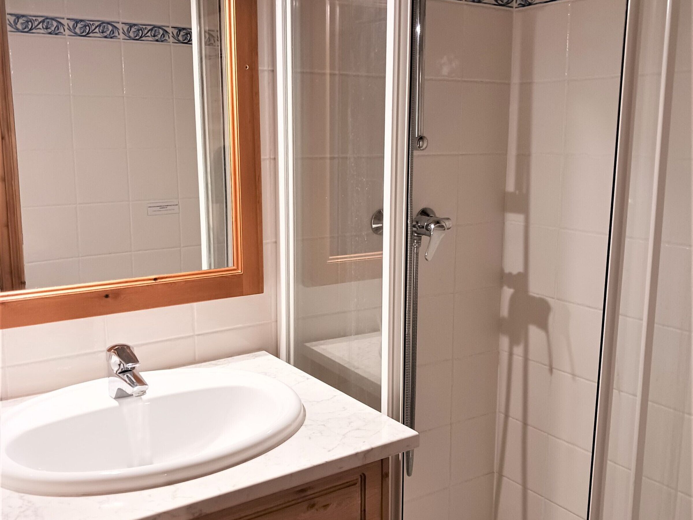 A bathroom with a white sink, a mirror with a wooden frame, and a glass-enclosed shower area.