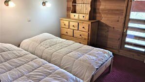 Un dormitorio con dos camas, un aparador de madera y una ventana con persianas.