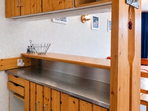 A kitchenette with wooden cabinets, a stainless steel countertop, and a hanging light fixture.
