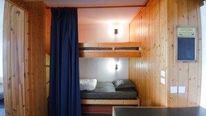 Pequeña habitación tipo cabaña de madera con literas, una cortina y un letrero que indica la zona de duchas.