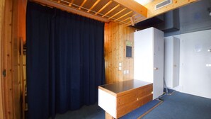 Una habitación con paredes de madera, una cortina oscura, un escritorio de madera, un armario blanco y una alfombra azul.