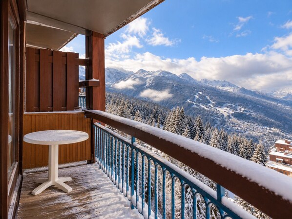 A balcony with a wooden railing and a small table, overlooking a snowy mountain landscape.
