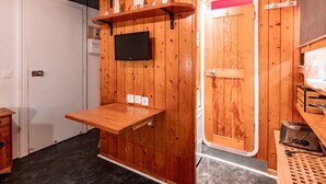 A compact room with wooden walls, a mounted TV, a small table, and a door with a red interior. - Cozy studio for 2, near slopes and shops with Wifi, parking Arc 1800 (Les Arcs 1800)