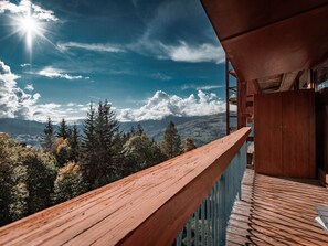 A wooden balcony with a view of a mountainous landscape and a clear sky.