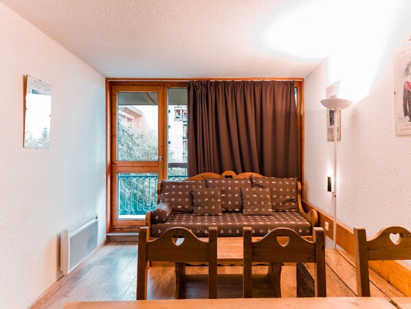 A cozy room with a wooden sofa, a small table, and a window with curtains.