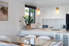 A modern kitchen with white cabinets, a glass dining table, and pendant lighting. - Waterfront Oasis in Runaway Bay (Runaway Bay)