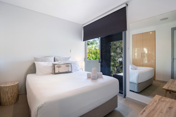A modern bedroom with a large bed, a wooden side table, and a view of a balcony.