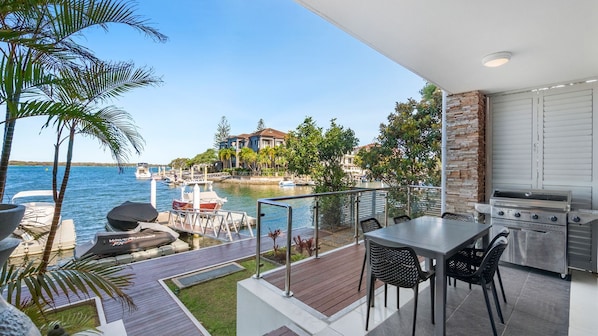 Une terrasse extérieure équipée d’un barbecue, d’une table à manger et de chaises, offrant une vue sur une marina avec des bateaux et des maisons.
