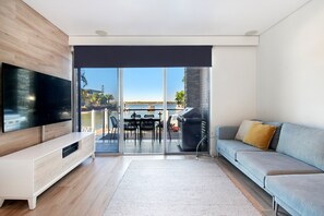 A modern living room with a flat-screen TV, a sofa, and a dining area with outdoor seating.