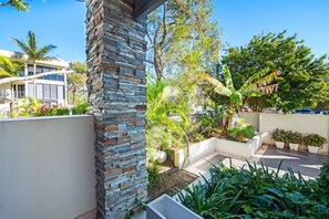 A modern building with a stone facade, surrounded by lush greenery and a clear blue sky.