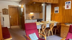 Ein gemütliches Zimmer mit Holzmöbeln, einem Esstisch für vier Personen und einer Küchenzeile mit Holzschränken und einem Wasserkocher.