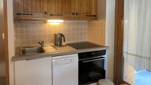 Eine kompakte Küche mit Holzausstattung, einem Geschirrspüler von Bosch, einem Backofen und einem Wasserkocher.