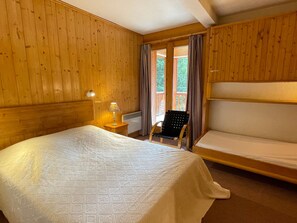 A wooden-paneled room with a bed, a chair, and a window with curtains.