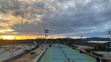 A tennis court complex with multiple courts, seating areas, and a parking lot.