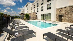 A hotel with a swimming pool, lounge chairs, and a stone facade.