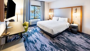 A hotel room with a bed, a desk, a chair, a TV, a window with curtains, and a nightstand with a lamp.