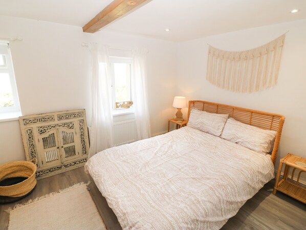 Une chambre à coucher avec un grand lit, une tête de lit en bois, une table de chevet avec une lampe, un panier en osier et un élément décoratif mural.