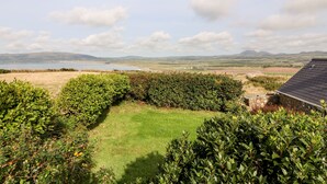 A view of a coastal landscape with a grassy area, hedges, and a stone building with a dark roof. - Sunstone (Pwllheli)