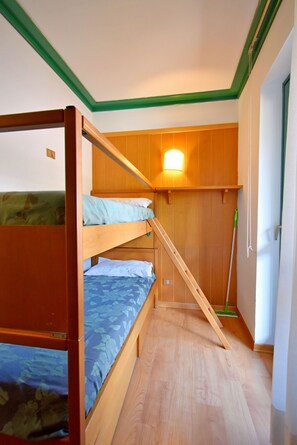 A compact room with a bunk bed, a wooden wardrobe, and a wall-mounted light fixture.