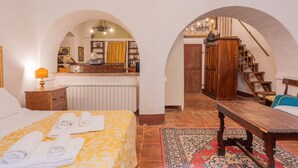 A bedroom with a bed, a wooden bench, a desk, and a mirror. - Palazzo Danesi (Montepulciano)