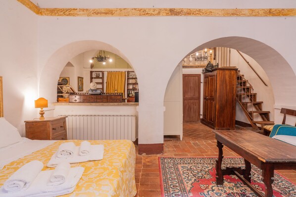 A bedroom with a bed, a wooden bench, a desk, and a mirror. - Palazzo Danesi (Montepulciano)