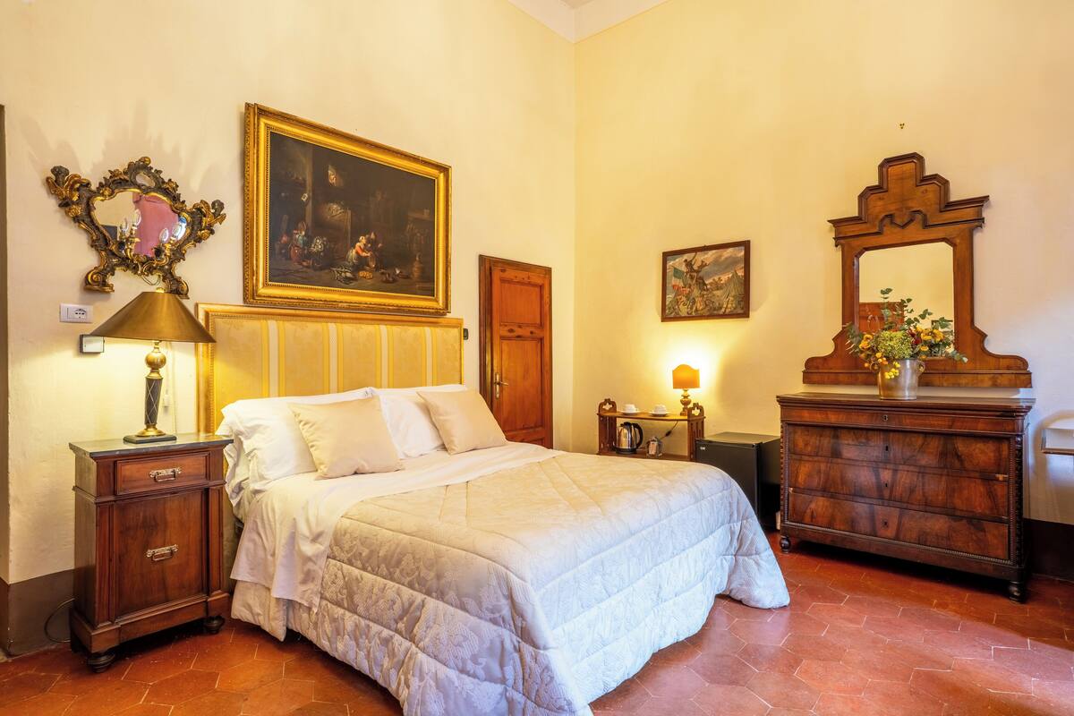 A bedroom with a large bed, a wooden dresser, a nightstand, a mirror, and a painting on the wall.